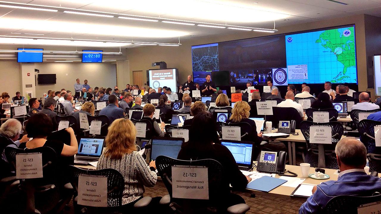 A control room full of communication employees with laptops and phones